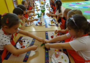 Dzieci dekorują lody w wafelku listkami mięty.
